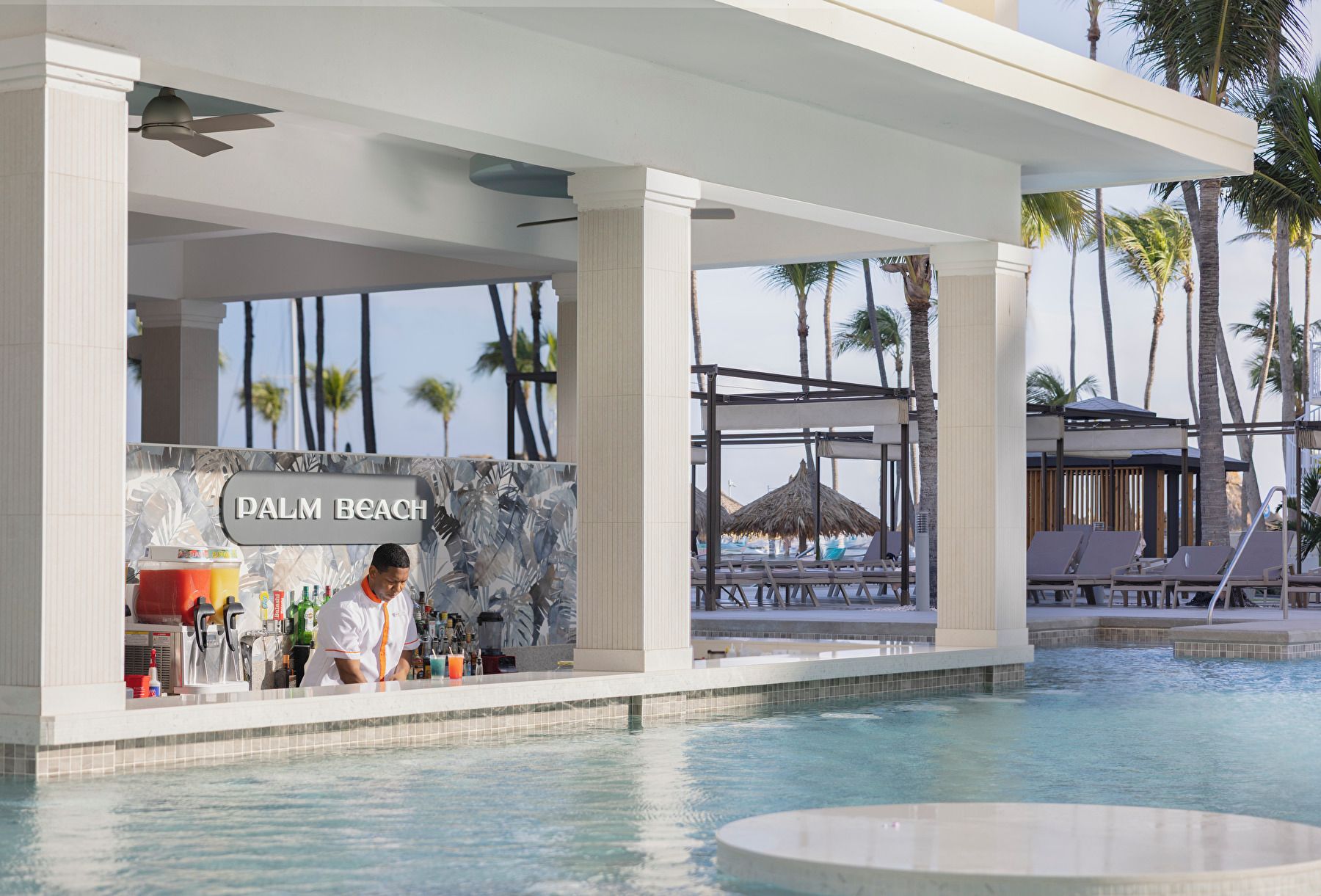 Een zwembadgedeelte met een bar, genaamd 'PALM BEACH', en ligbedden.