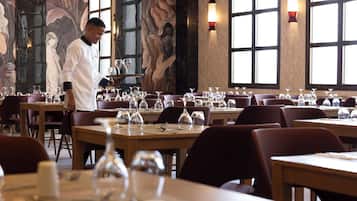 A restaurant interior with tables set for dining, a waiter carrying a tray, and decorative wall art.