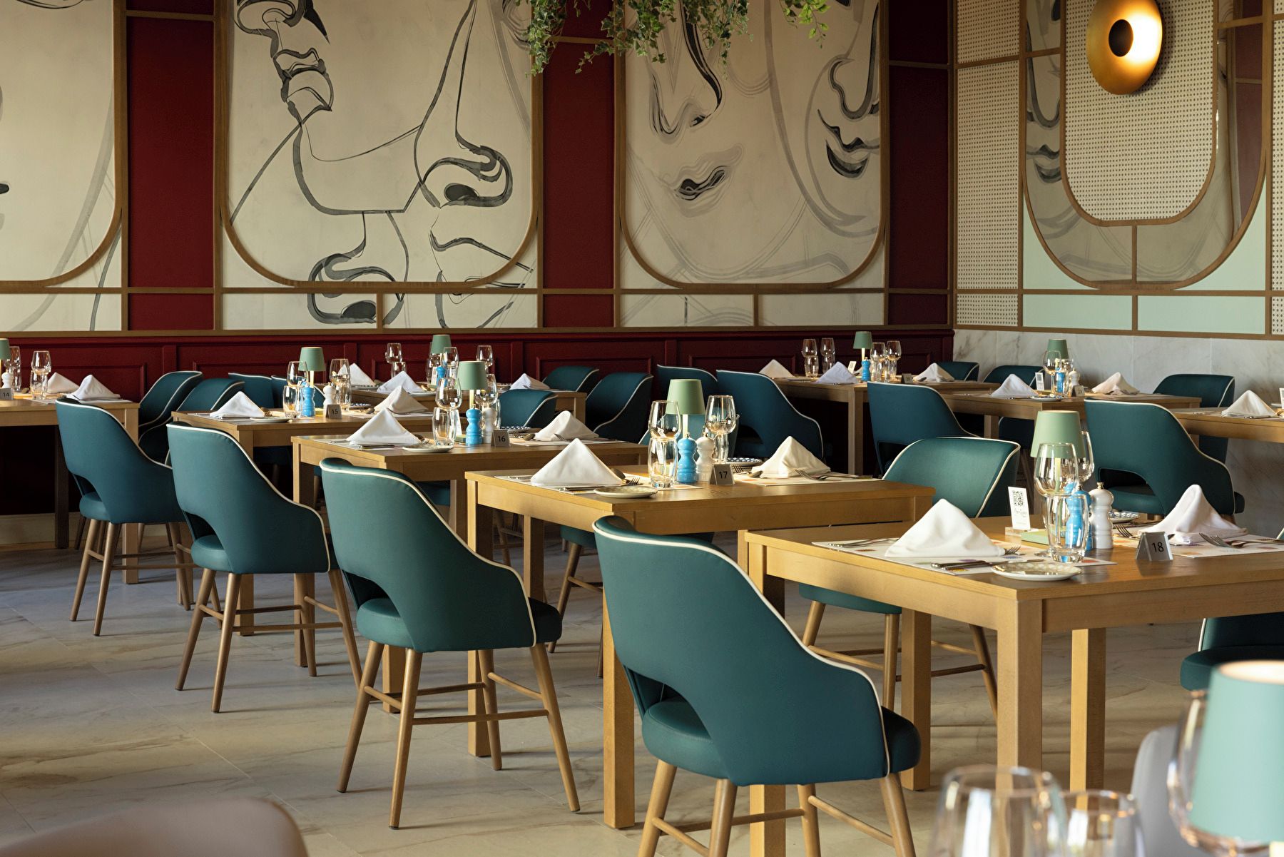 A restaurant with tables set for dining, teal chairs, and a wall with abstract art.