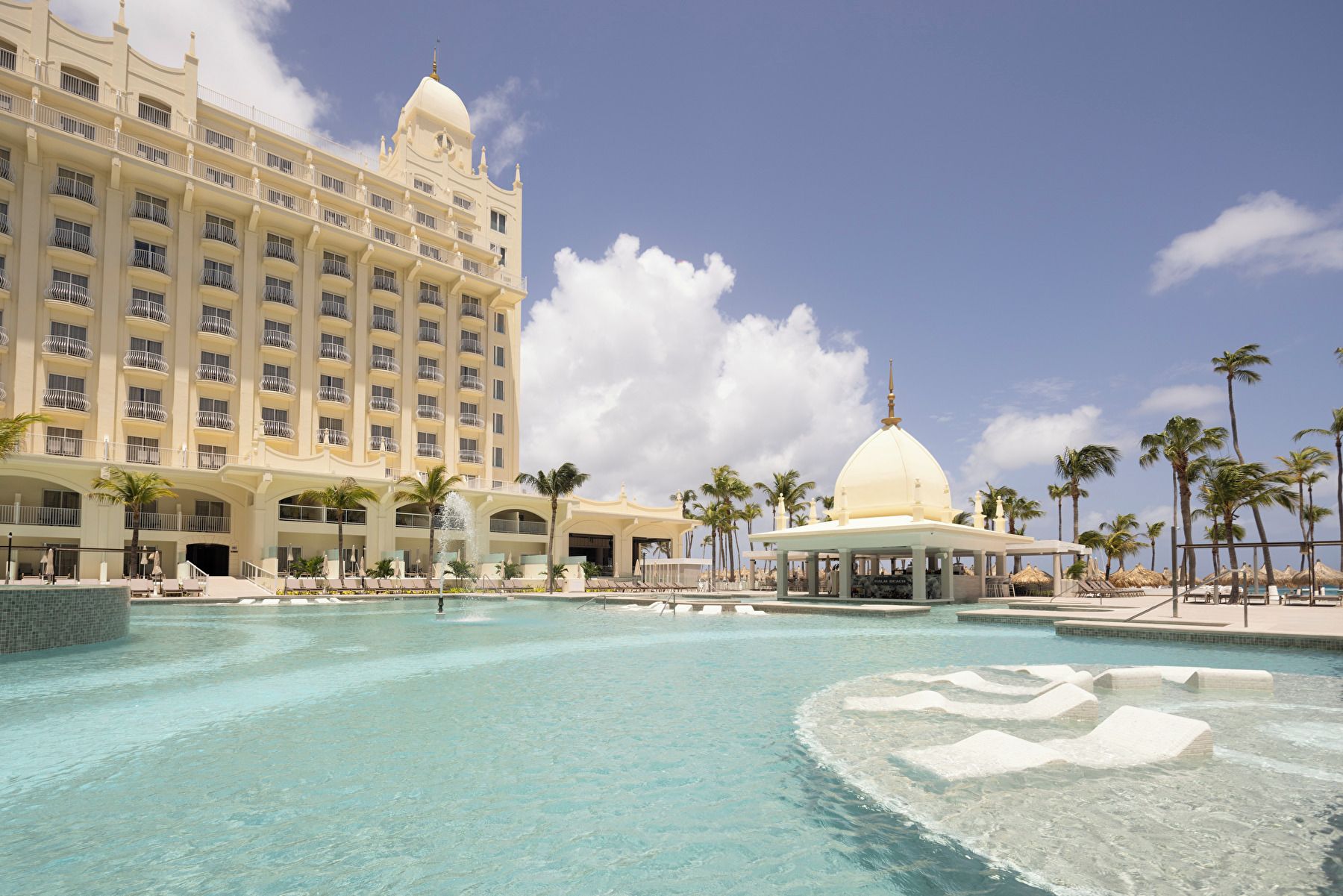 Un hotel con una piscina grande, palmeras y una estructura en forma de cúpula.