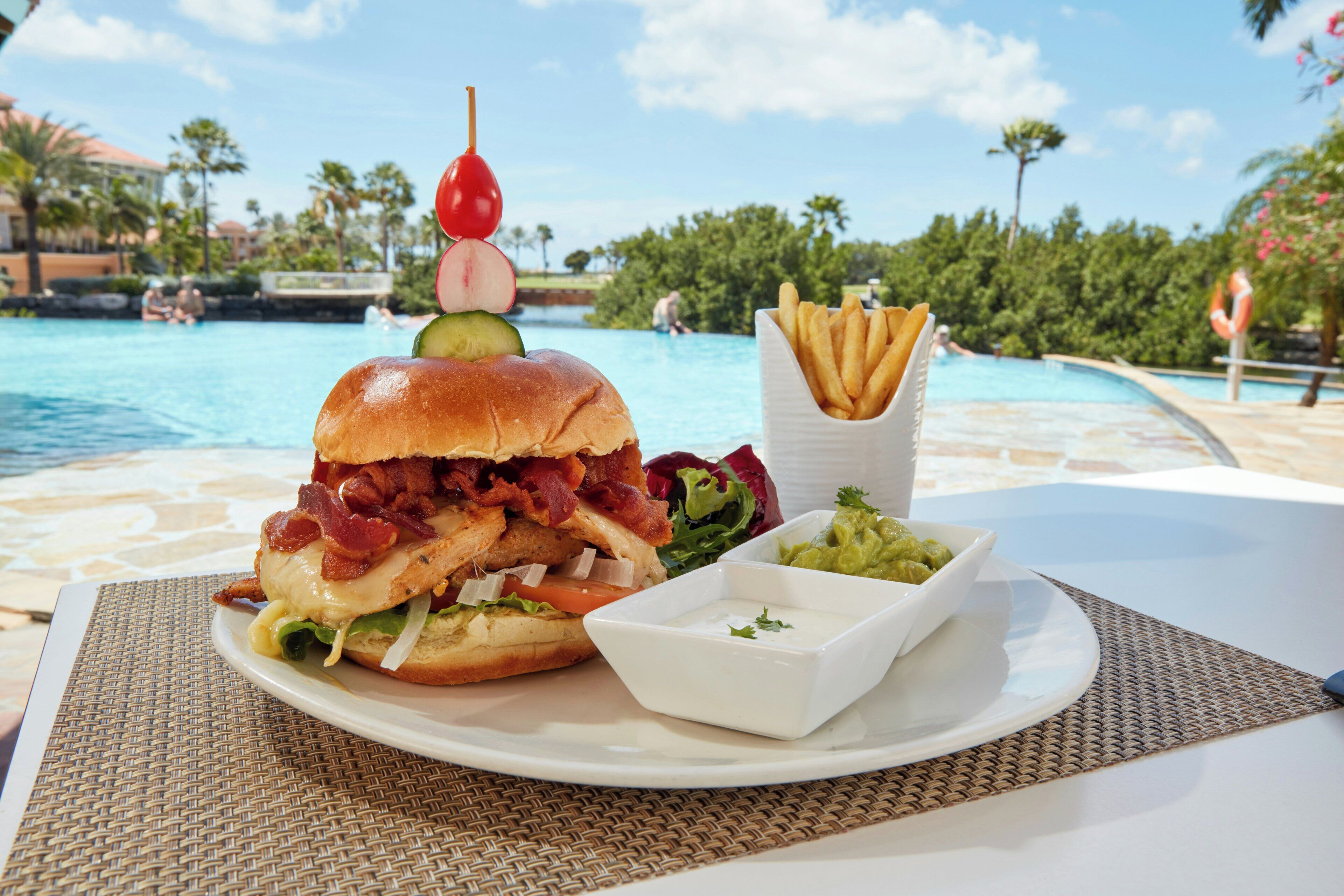 Comida con hamburguesa, papas fritas y ensalada junto a una piscina.