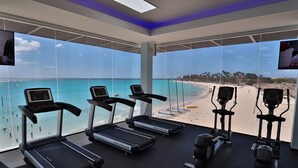 A gym with treadmills and elliptical machines, large windows with a beach view. - Divi Village Golf & Beach Resort (Oranjestad)