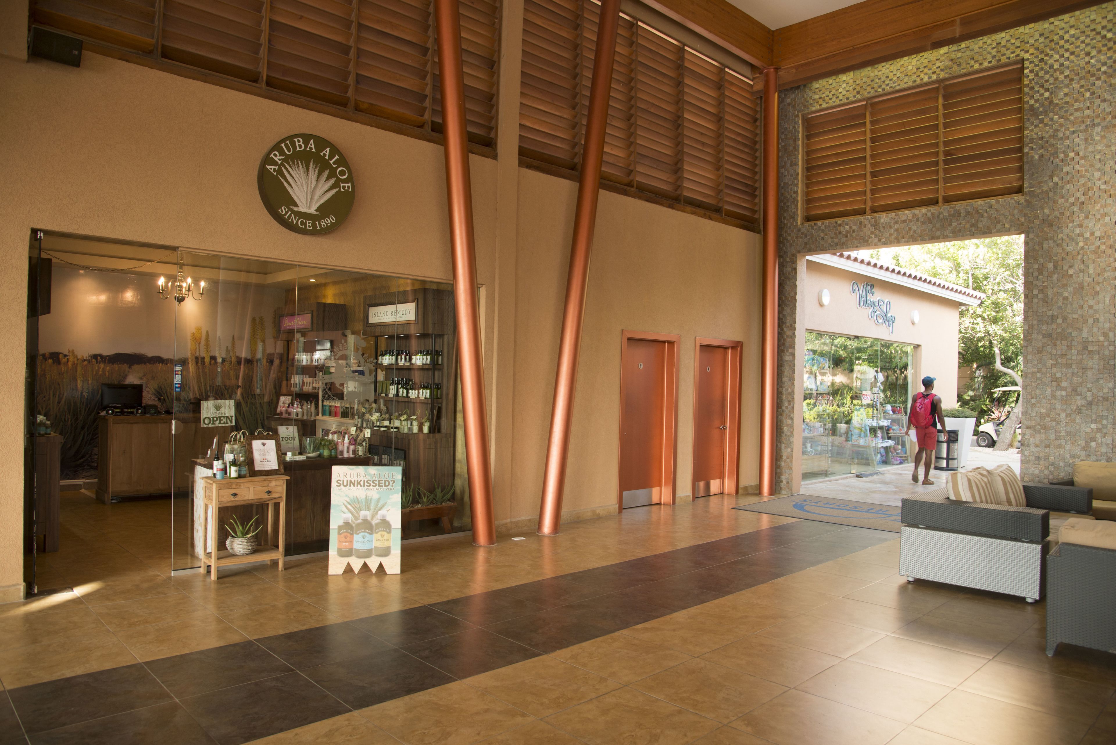 A lobby with a reception desk, a store named 'Aruba Aloe', and a seating area with a view of the outside.