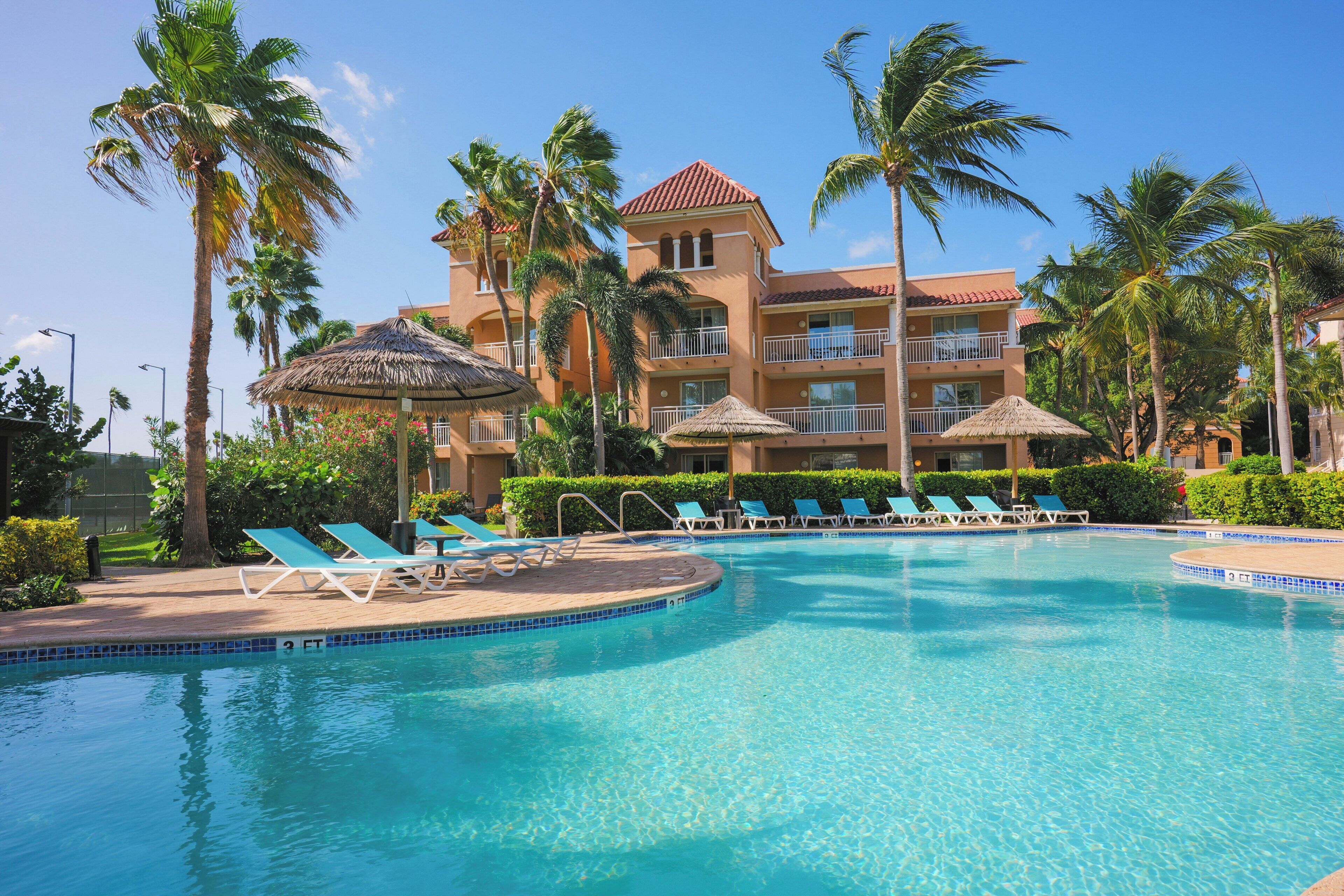 Un hotel con piscina, palmeras y sillas de descanso.