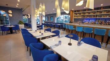 A restaurant with blue chairs, white tables, and a bar with shelves of bottles.