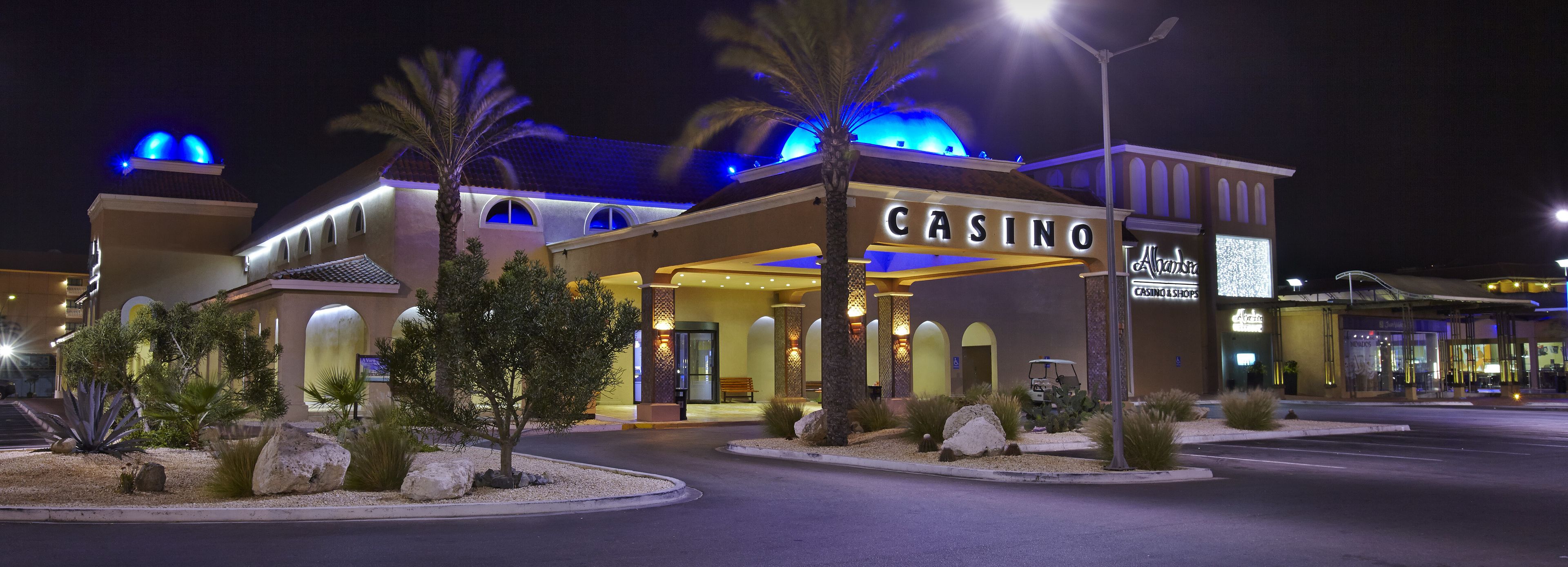 A casino building with a prominent entrance, palm trees, and a well-lit facade.