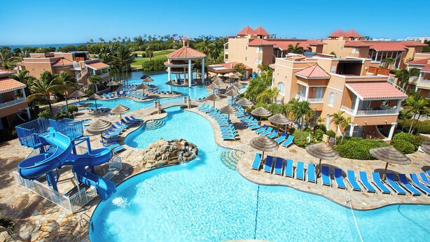A resort with a large swimming pool, lounge areas, and a view of the ocean. - Divi Village Golf & Beach Resort (Oranjestad)