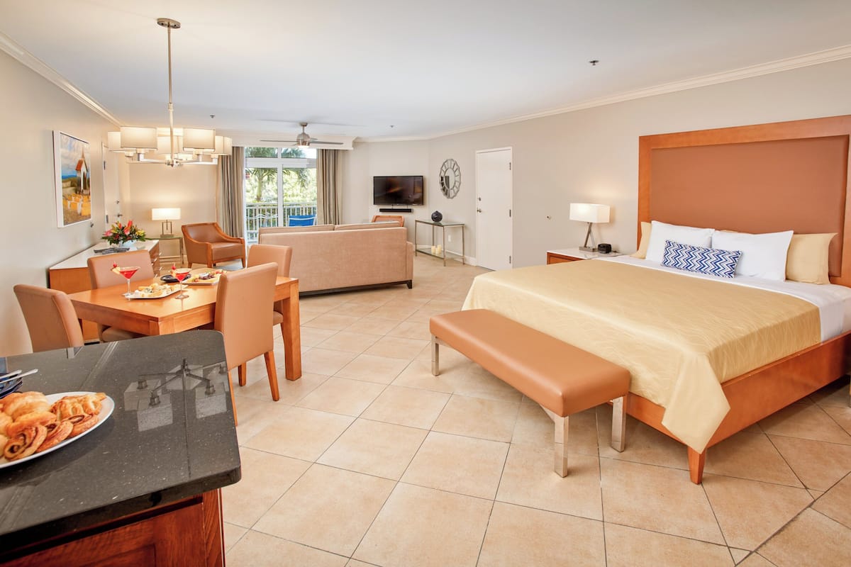 A hotel room with a bed, a desk with a chair, a sofa, a TV, and a dining area with a table and chairs.