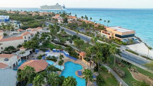 A resort with a swimming pool, palm trees, and a cruise ship in the background. - Divi Village Golf & Beach Resort (Oranjestad)