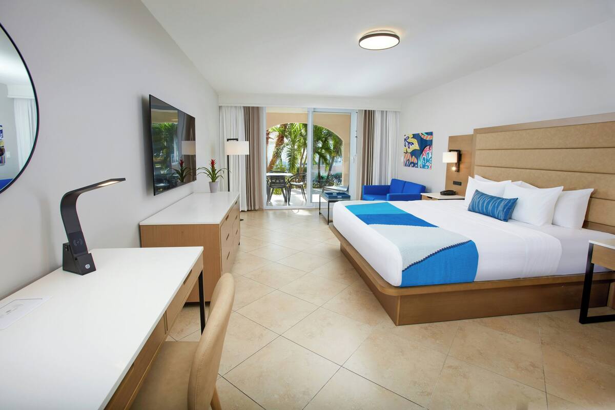 A hotel room with a bed, desk, chair, and a view of the outdoors.