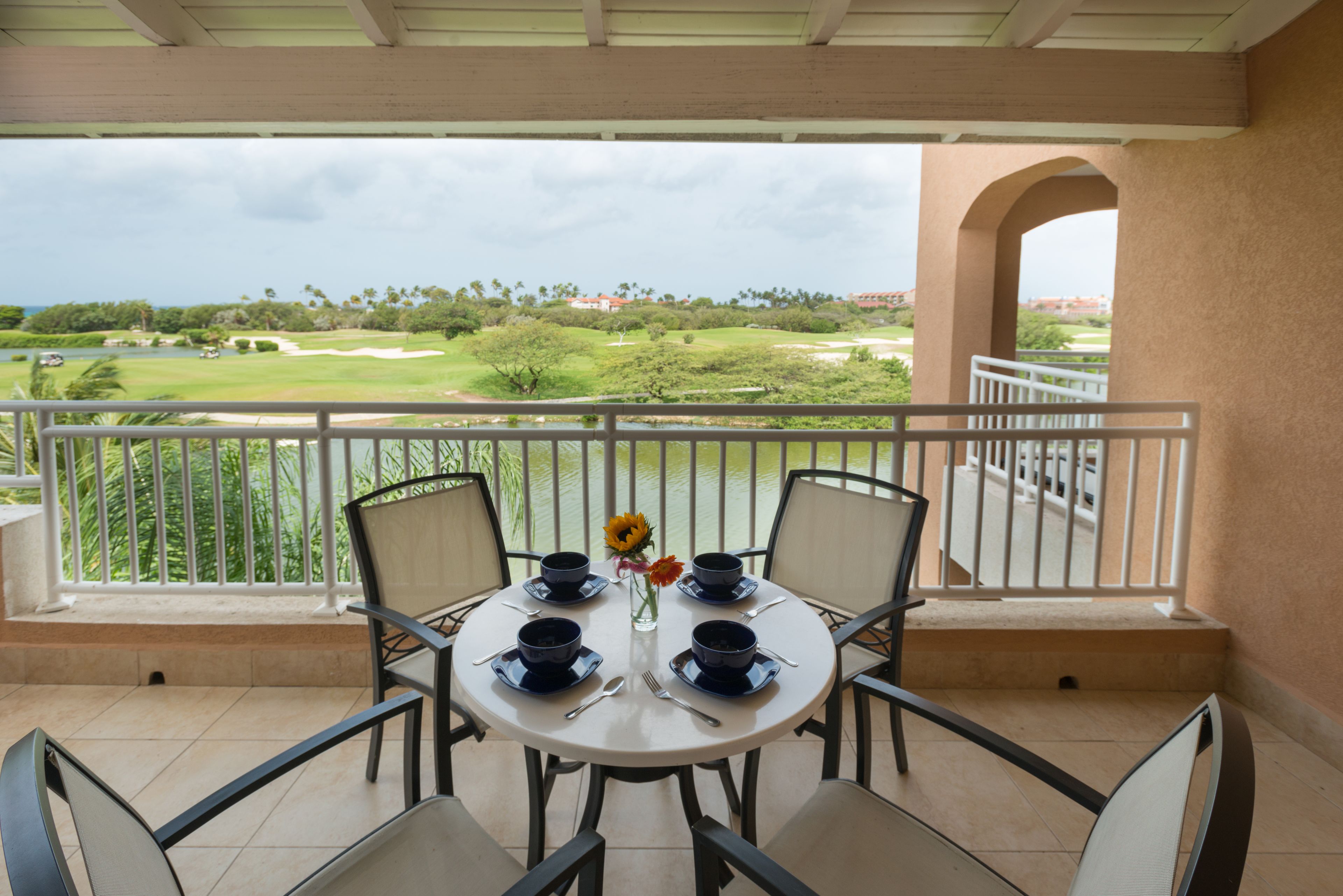 A round table with four blue bowls and a vase with flowers on a balcony overlooking a golf course.