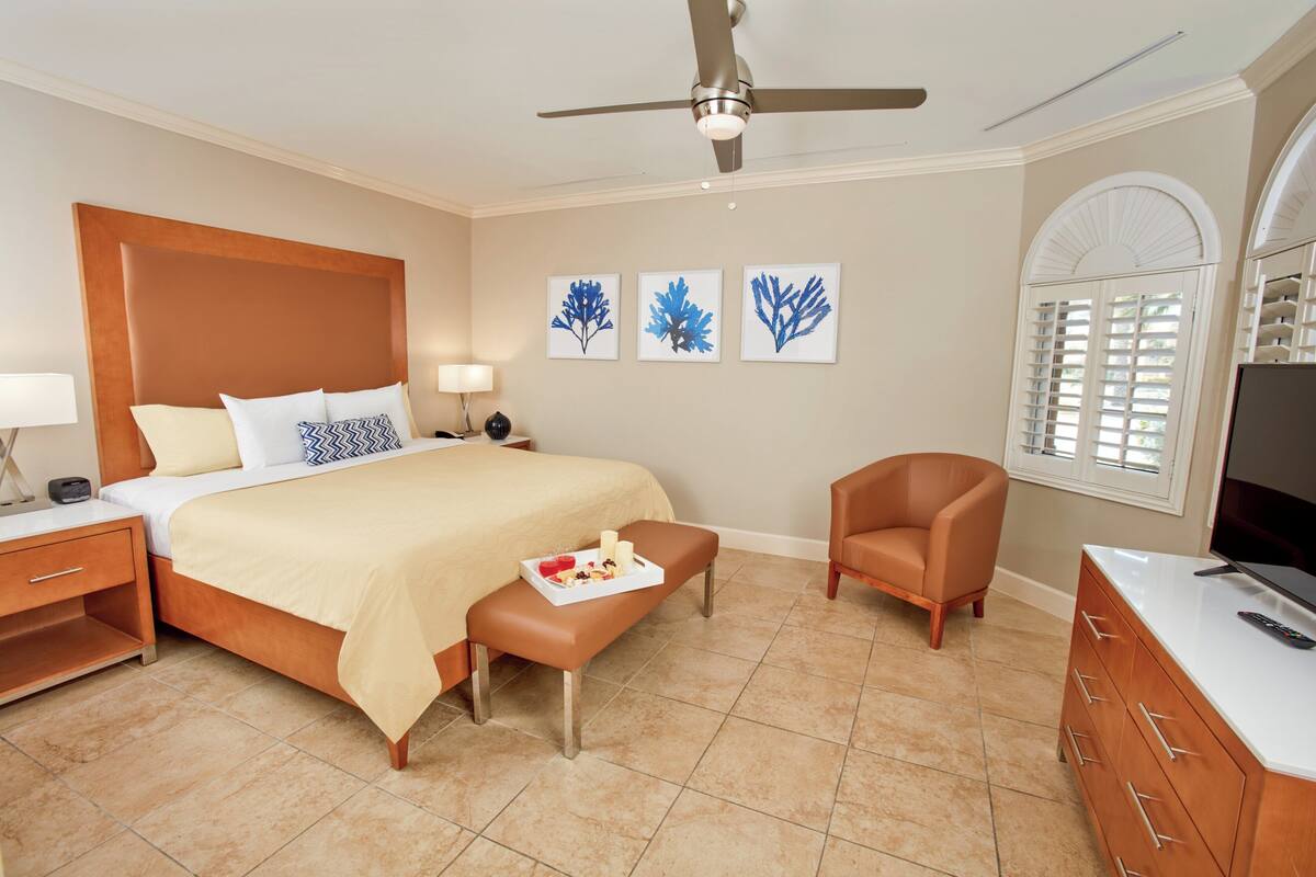 A hotel room with a bed, a chair, a TV, a desk, and artwork on the wall.