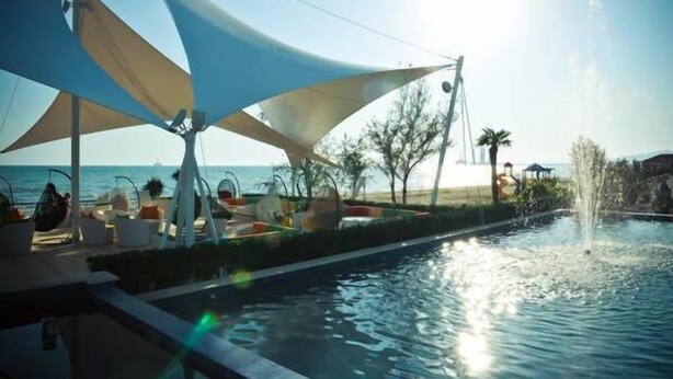 Zona de piscina con fuente, sillas de descanso y vista al mar.