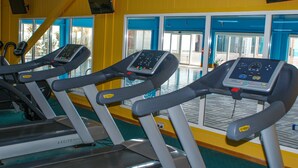 Tres bicicletas estáticas en un gimnasio con paredes amarillas y ventanas amplias.