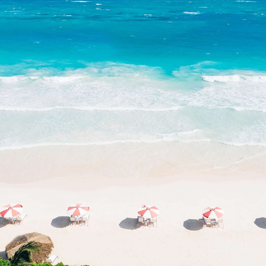 A beach with white sand and turquoise water. There are several beach umbrellas and lounge chairs arranged in a row.