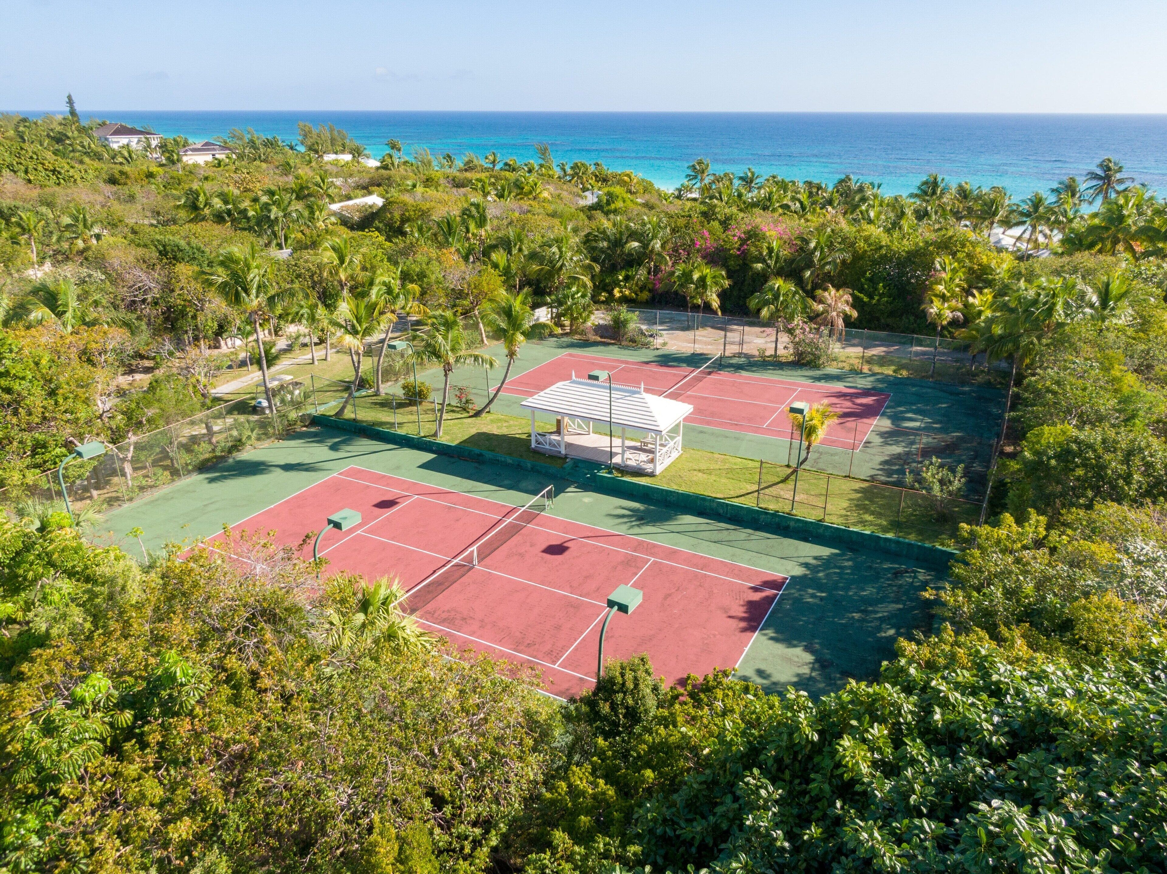 Un complesso di campi da tennis con più campi, circondato da vegetazione rigogliosa e vista sull'oceano.