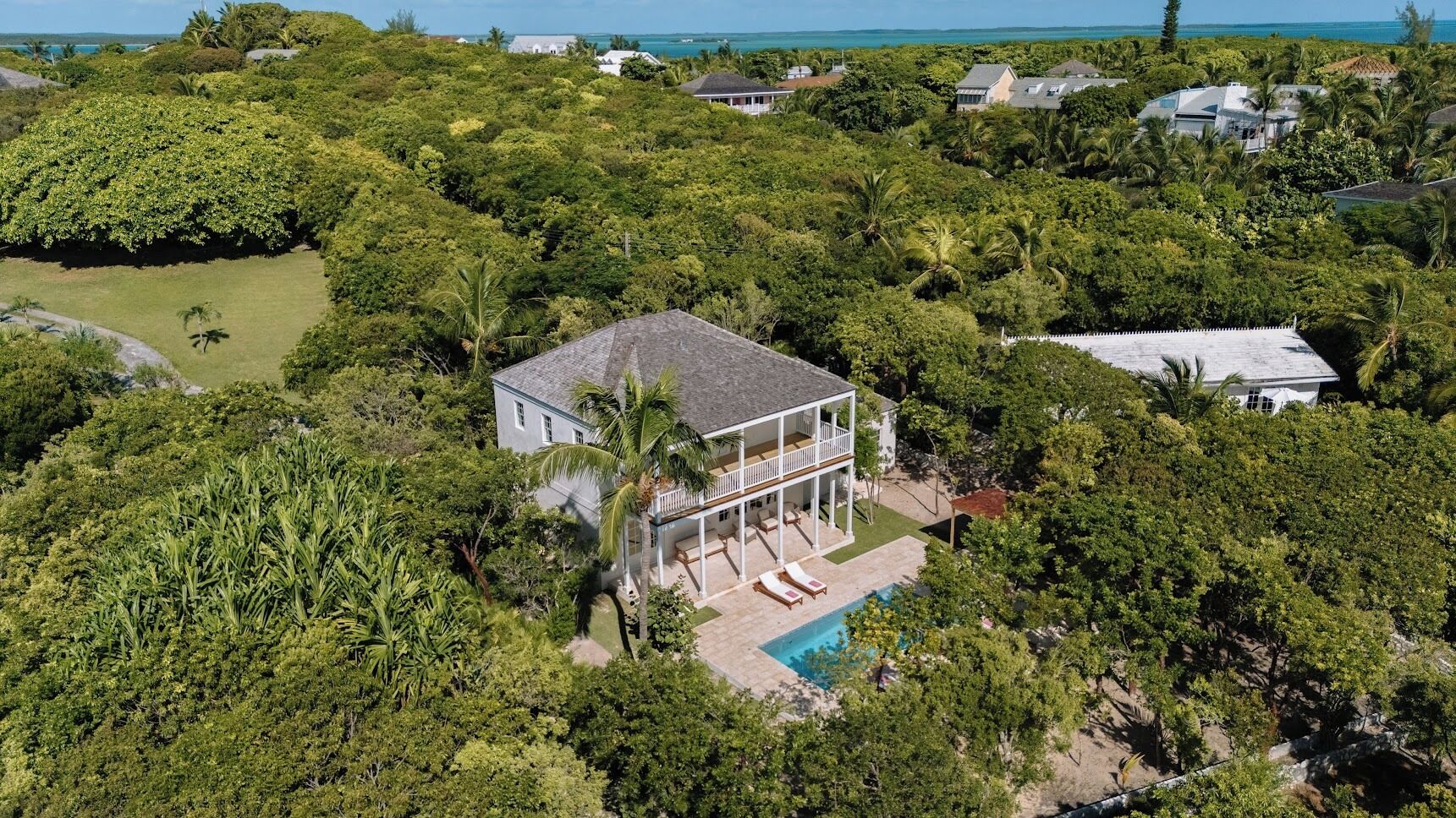 A large house surrounded by dense tropical vegetation, with a visible swimming pool and multiple balconies.