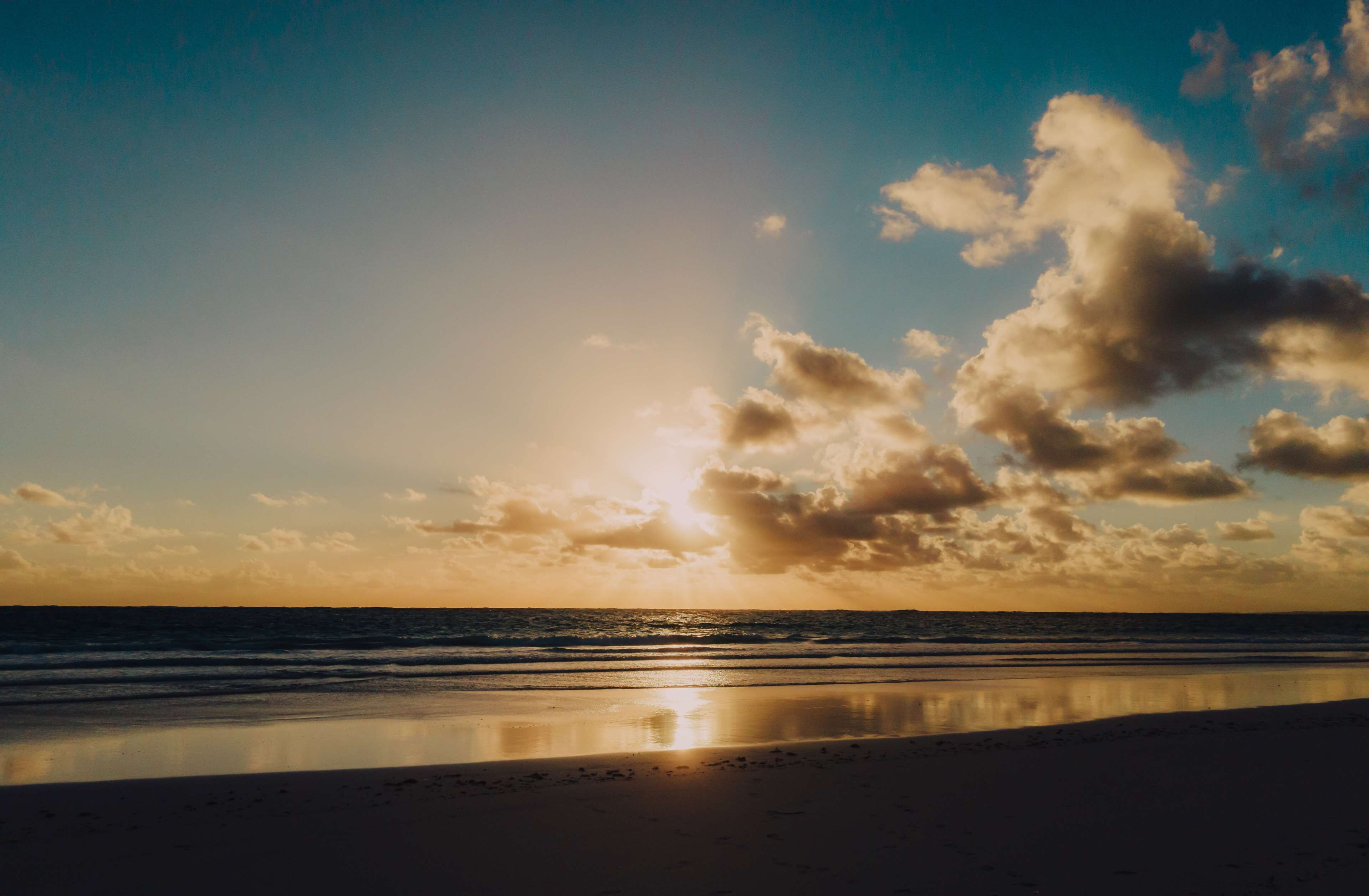 A beach with a calm sea and a clear sky with clouds.