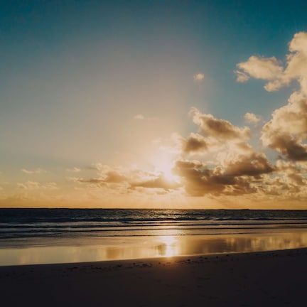 A beach with a calm sea and a clear sky with clouds.