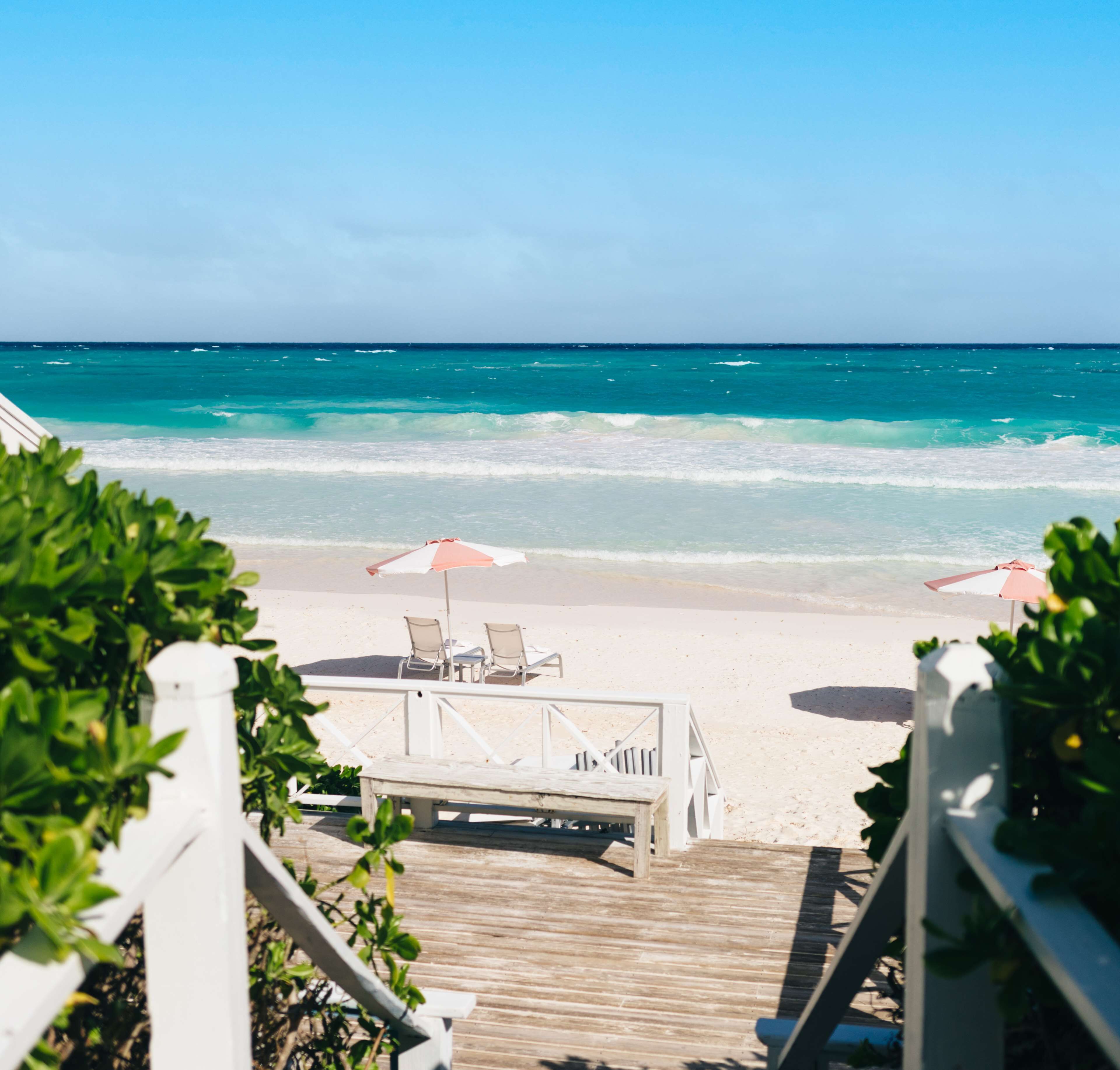 Une terrasse en bois menant à une plage, avec deux parasols et des chaises longues.