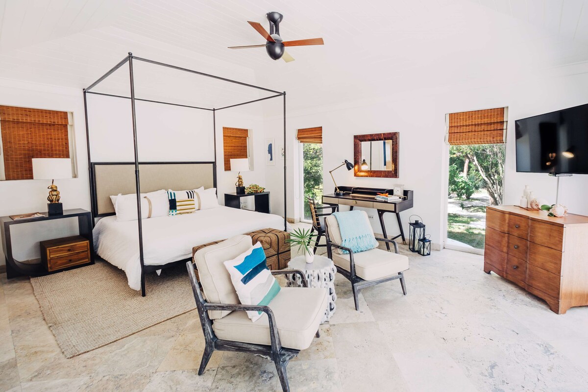 Un dormitorio espacioso con cama con dosel, una zona de estar con sofá y sillones, un televisor y un aparador de madera.