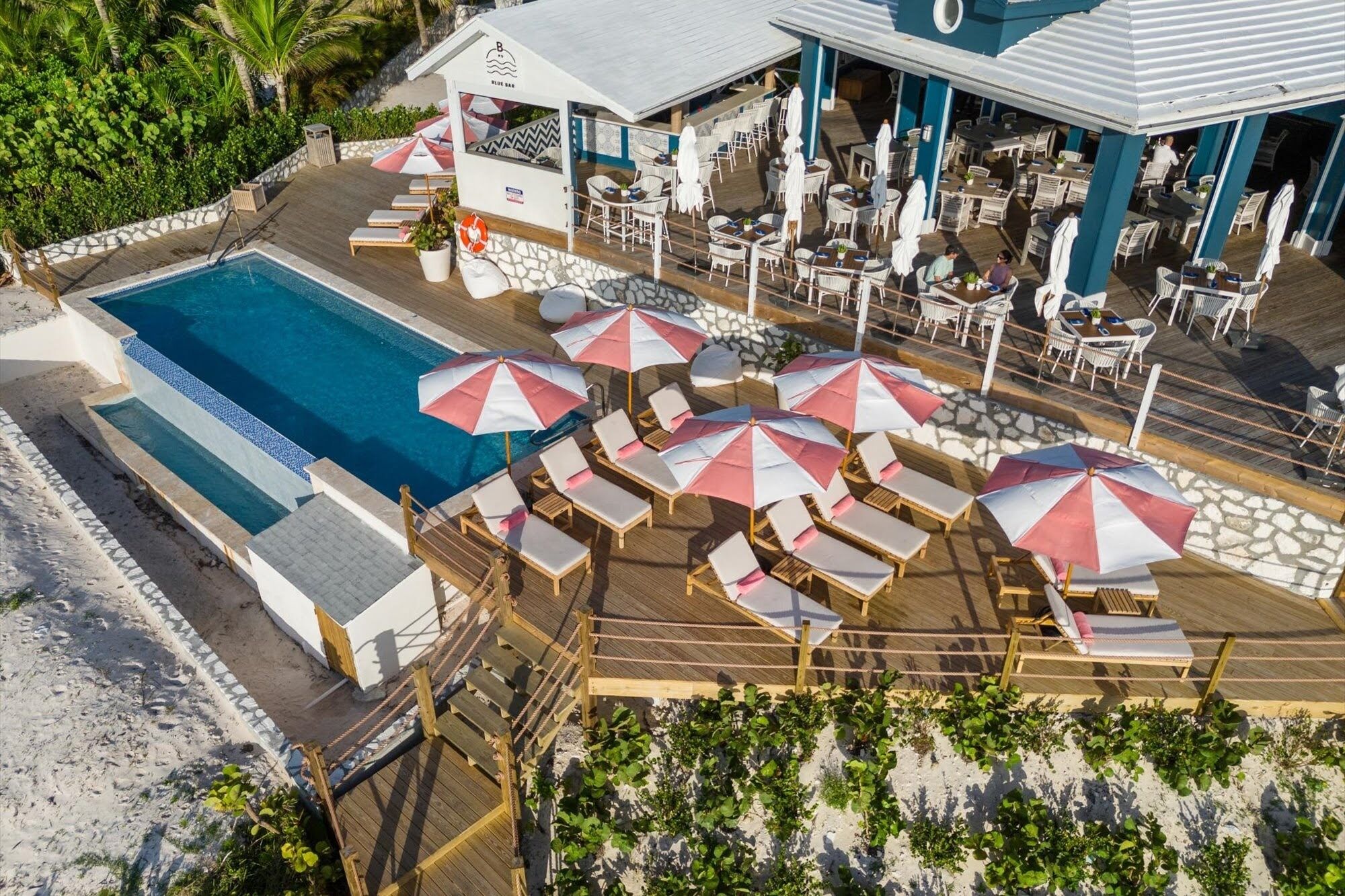 A poolside area with lounge chairs and umbrellas, a bar, and a pool.