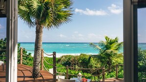 A wooden deck with a rope barrier, a palm tree, and a view of the ocean. - Pink Sands Resort (Dunmore Town)