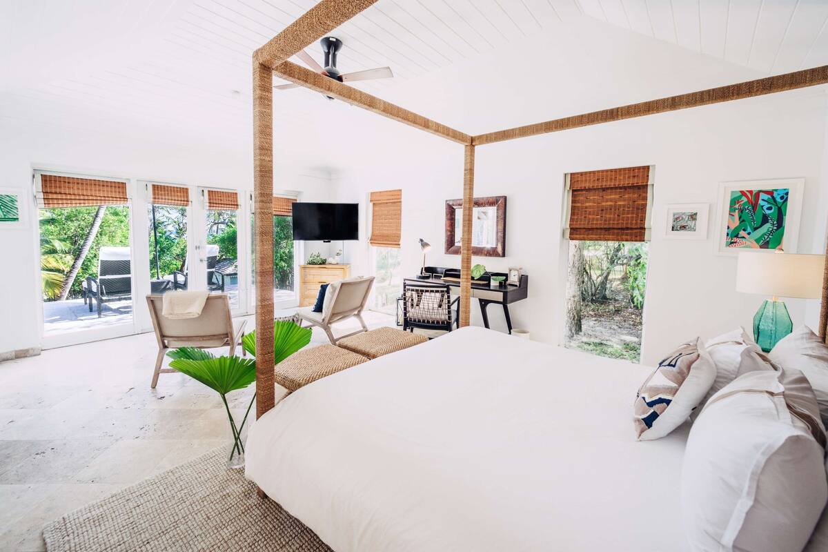 A spacious bedroom with a four-poster bed, a desk, and a television.