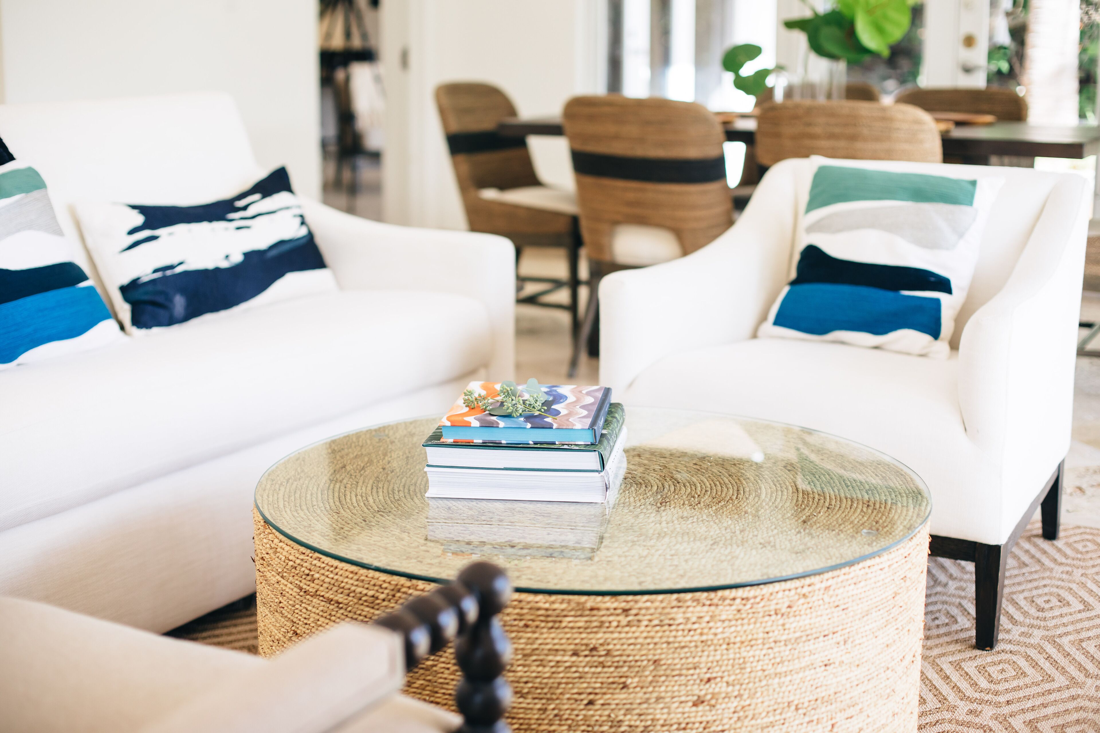 Un salon avec un canapé blanc, une table basse en verre et une table d’appoint en osier.