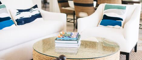 Un salon avec un canapé blanc, une table basse en verre et une table d’appoint en osier.