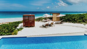 A poolside area with lounge chairs, umbrellas, and a wooden structure near the water. - Pink Sands Resort (Dunmore Town)