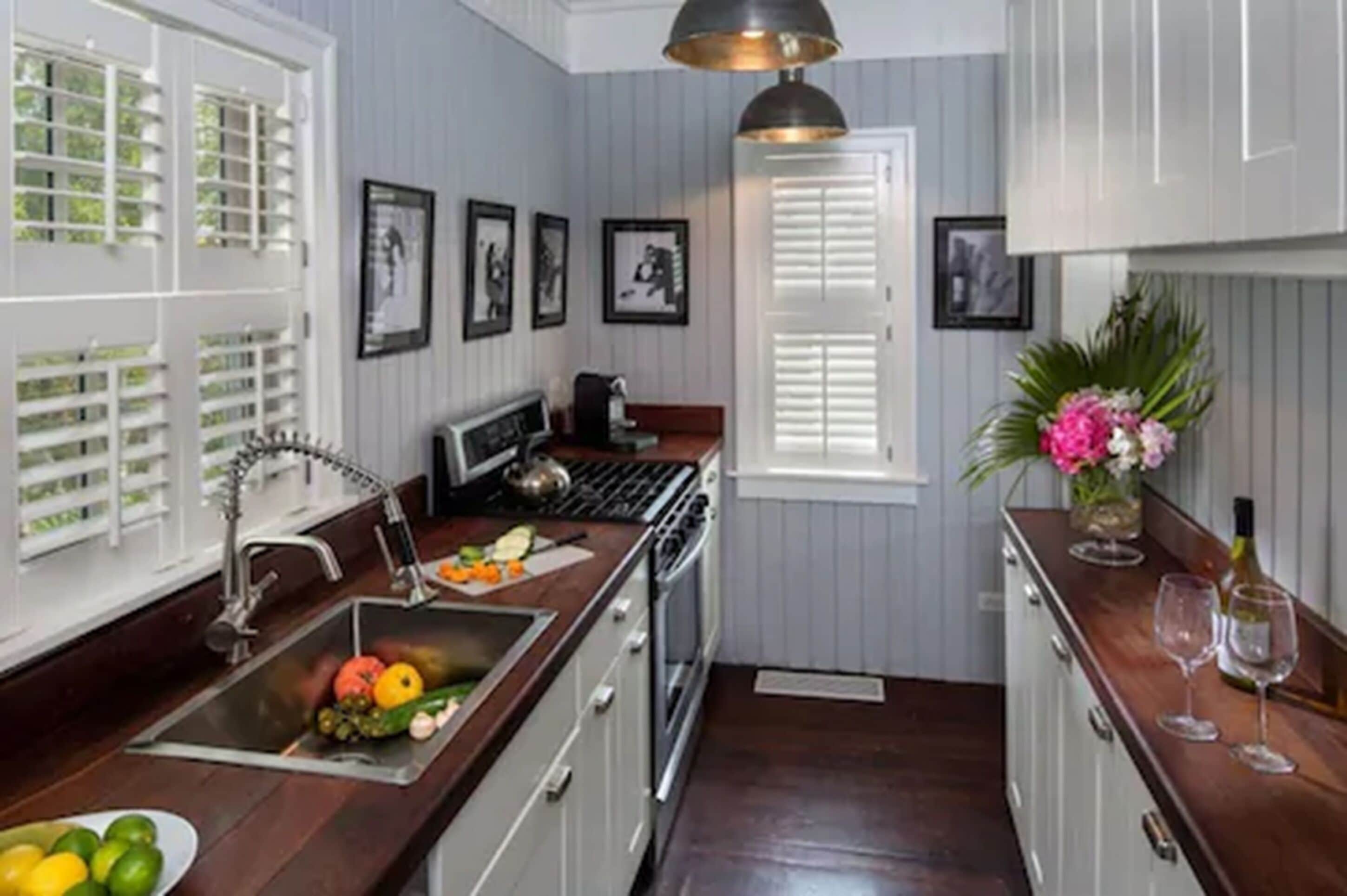 Una cocina con armarios blancos, una encimera de madera, un fregadero, una estufa y una lámpara colgante.