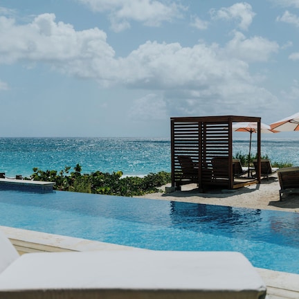 A poolside area with lounge chairs and umbrellas, overlooking the ocean.