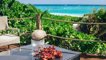 A glass-top table with a coconut shell and red berries on a wooden deck overlooking a beach.