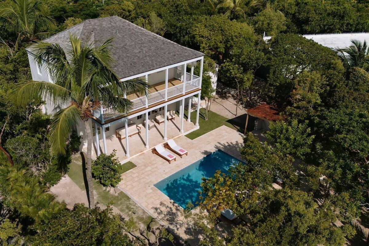 A two-story house with a balcony, a swimming pool, and lush greenery surrounding the property.