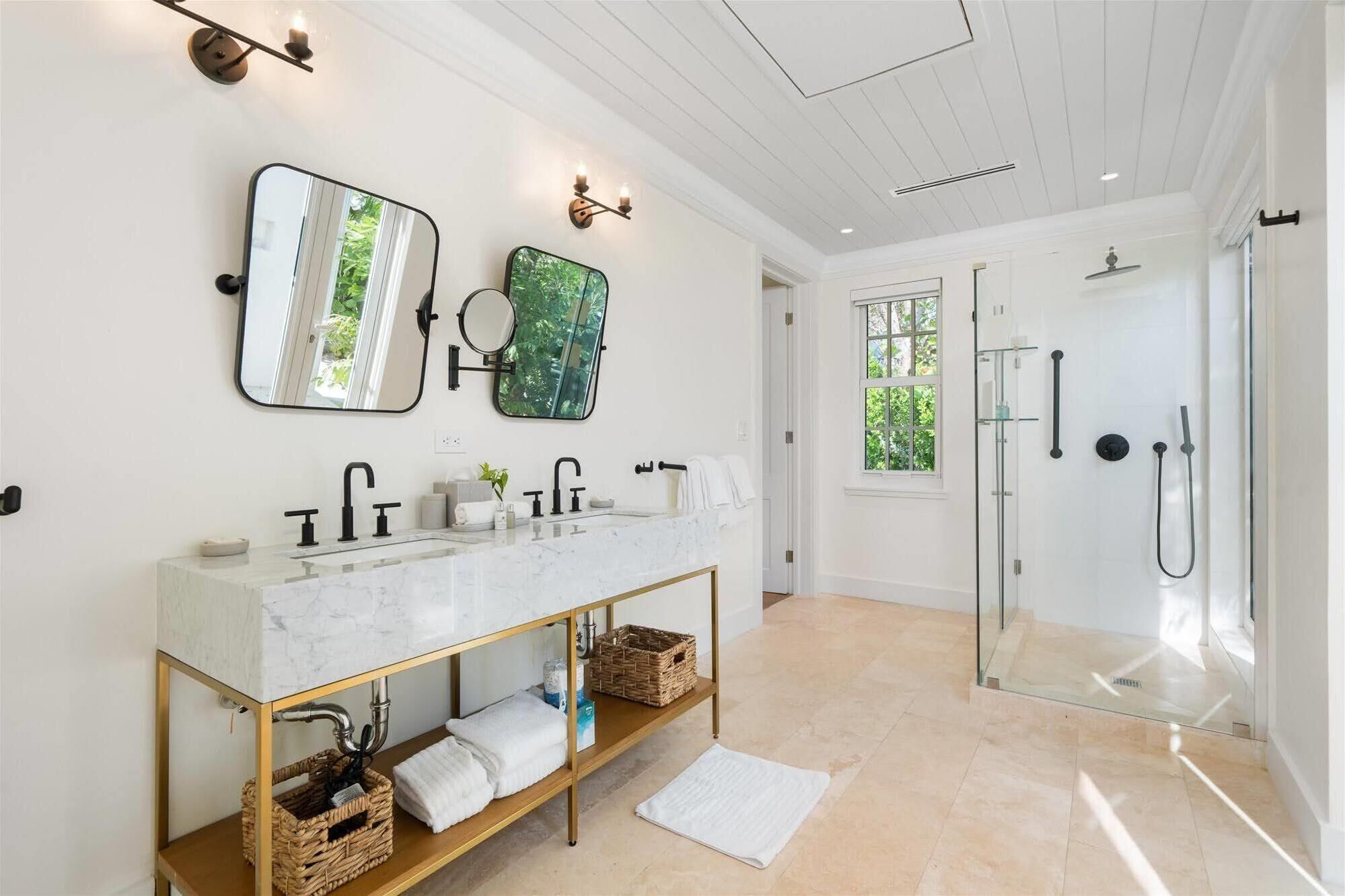 A modern bathroom with a marble vanity, a large mirror, and a glass-enclosed shower.