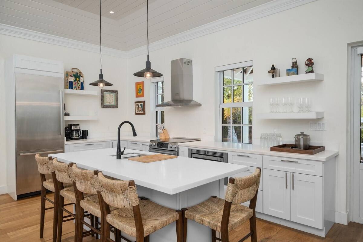 A modern kitchen with white cabinetry, a large island with bar stools, pendant lighting, and a stainless steel refrigerator.