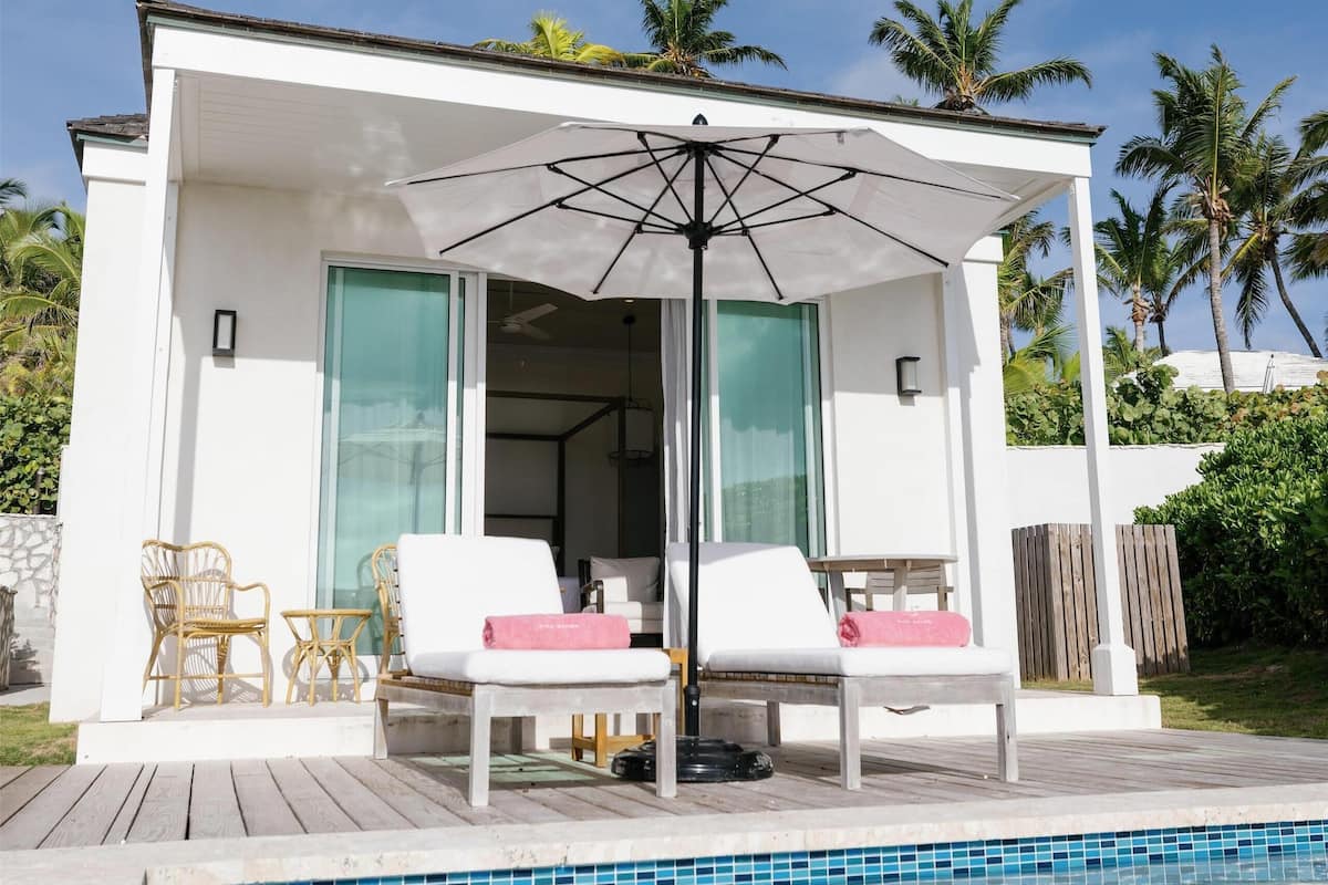 A modern poolside area with a white building, two lounge chairs, a table, and an umbrella.