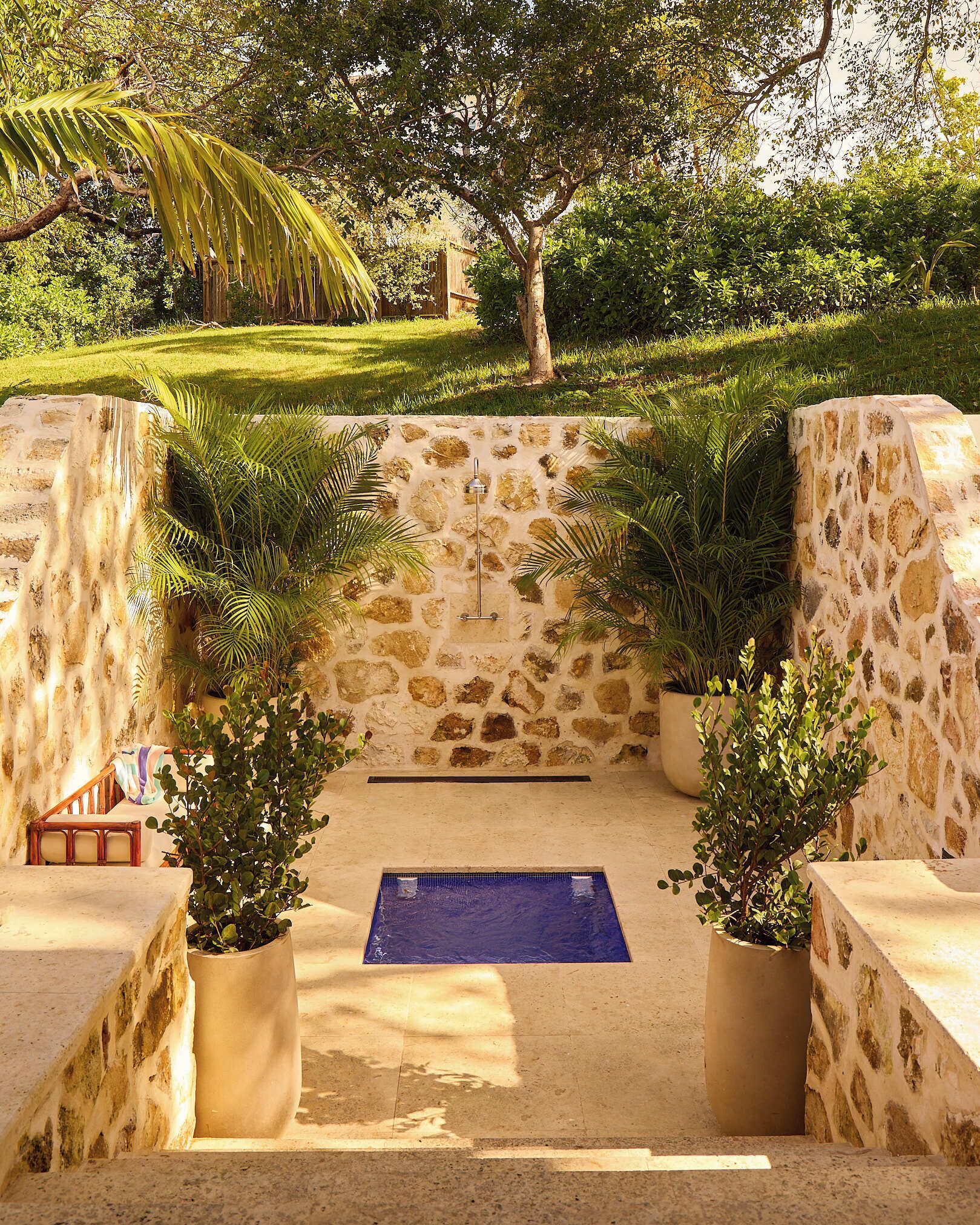 A stone-walled pool area with a blue pool, surrounded by potted plants and a wooden bench.
