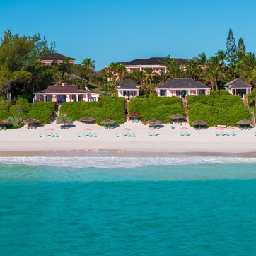 A beachfront property with multiple villas, a sandy beach, and a clear blue sea.