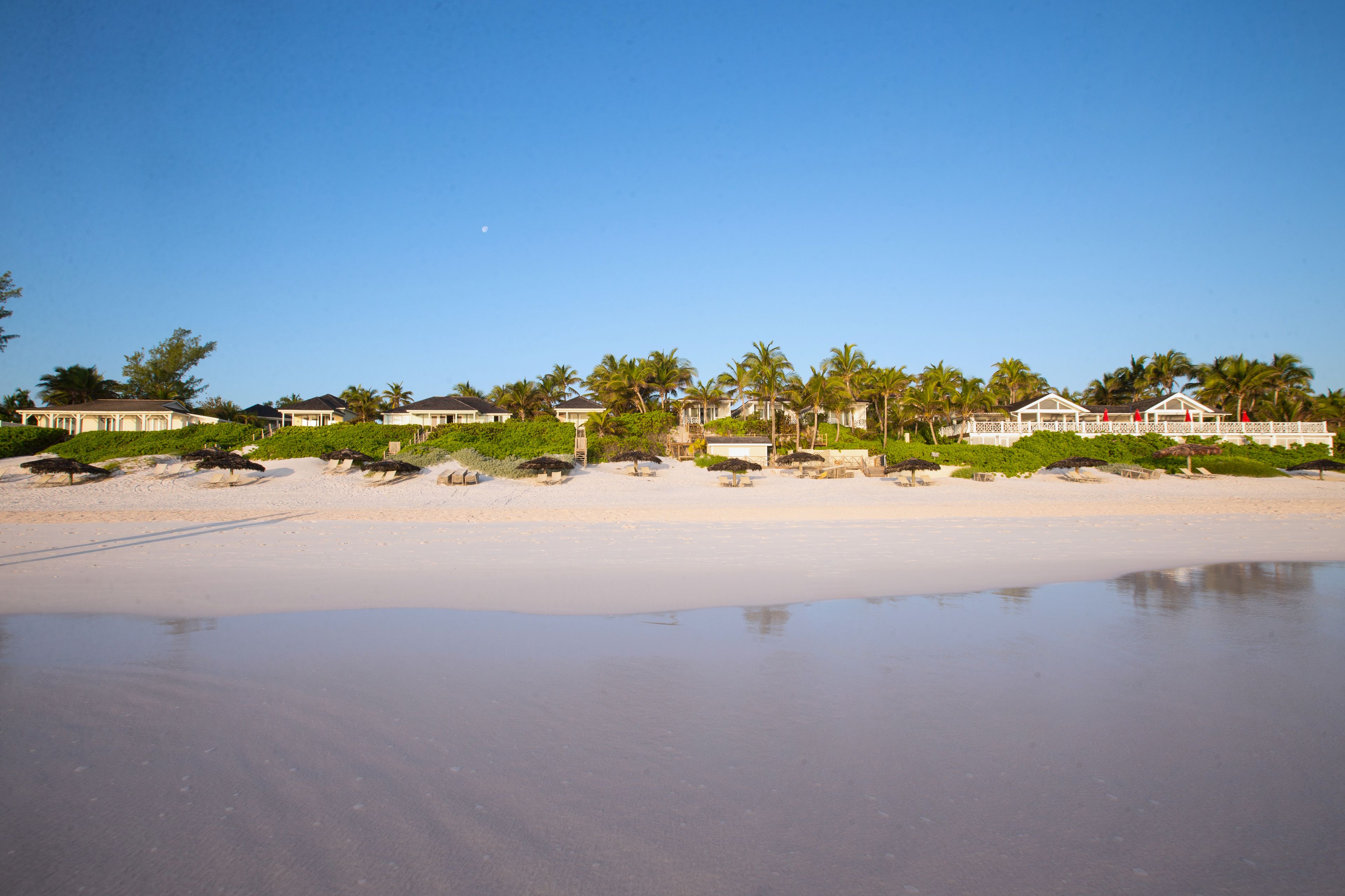 Eine Strandimmobilie mit mehreren Häusern, einem Sandstrand und Palmen.