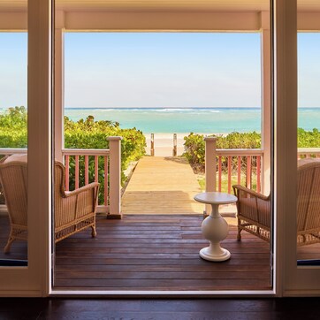 A wooden deck with wicker furniture and a view of the ocean.
