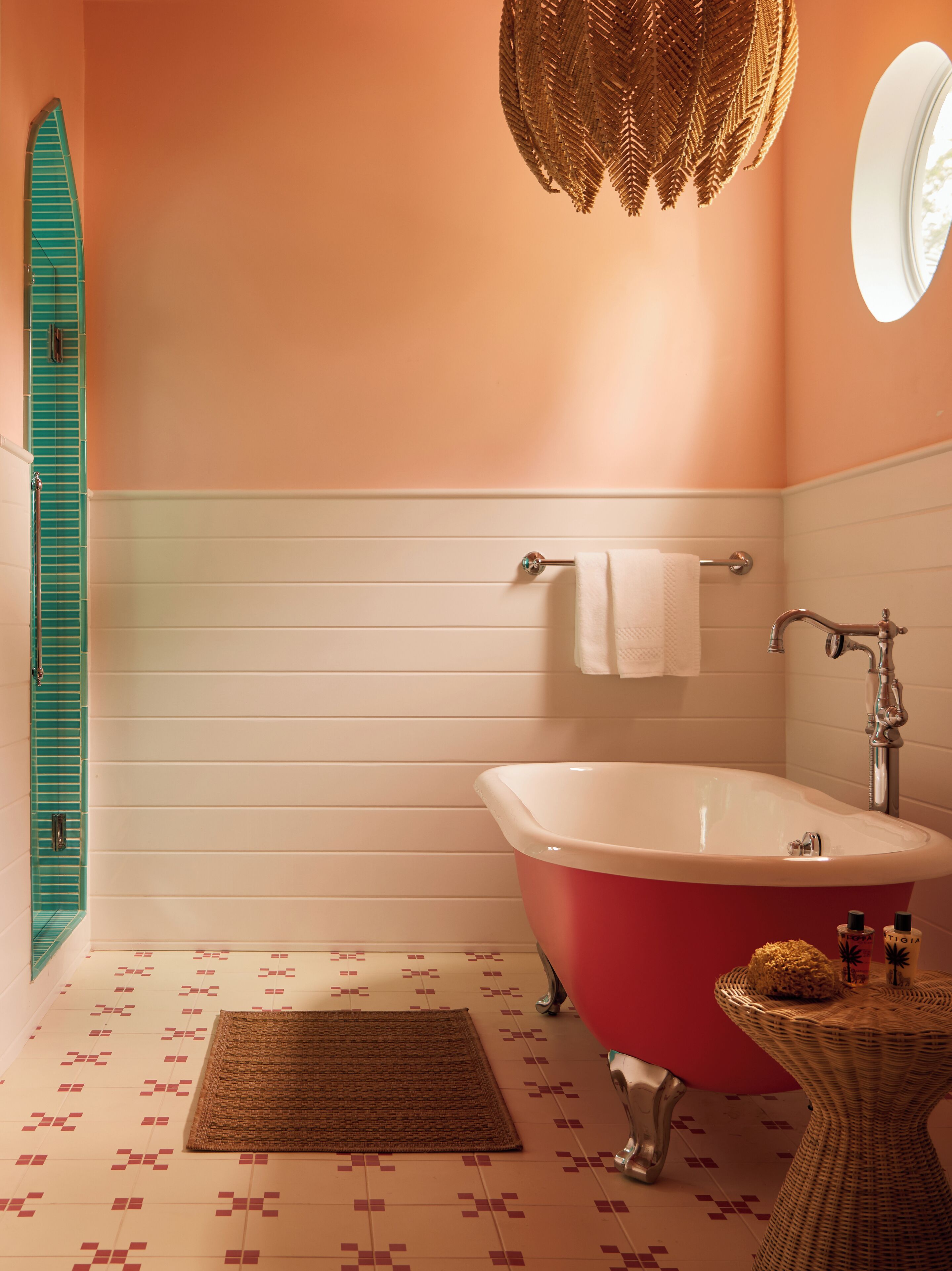 A bathroom with a red bathtub, a white sink, a round mirror, and a green window shutter.