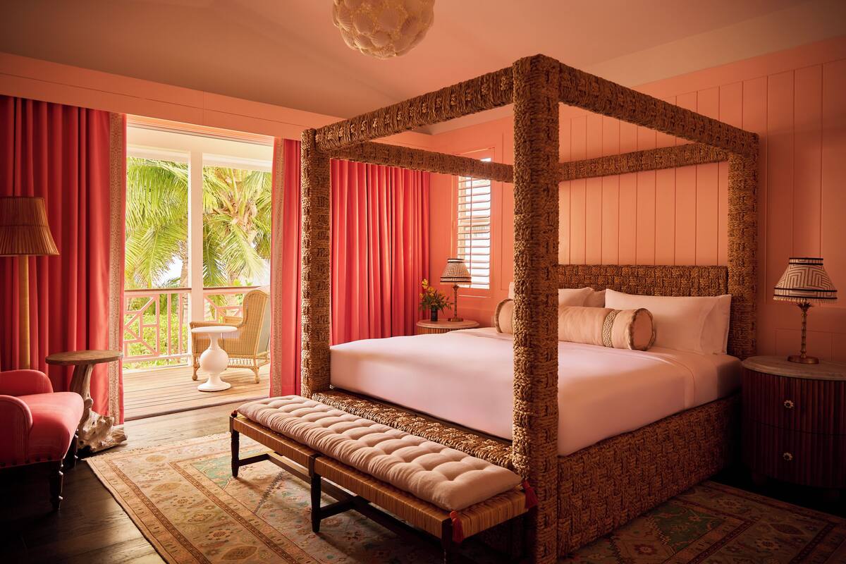 A four-poster bed with a bench, a small round table, and a chair in a room with a balcony.