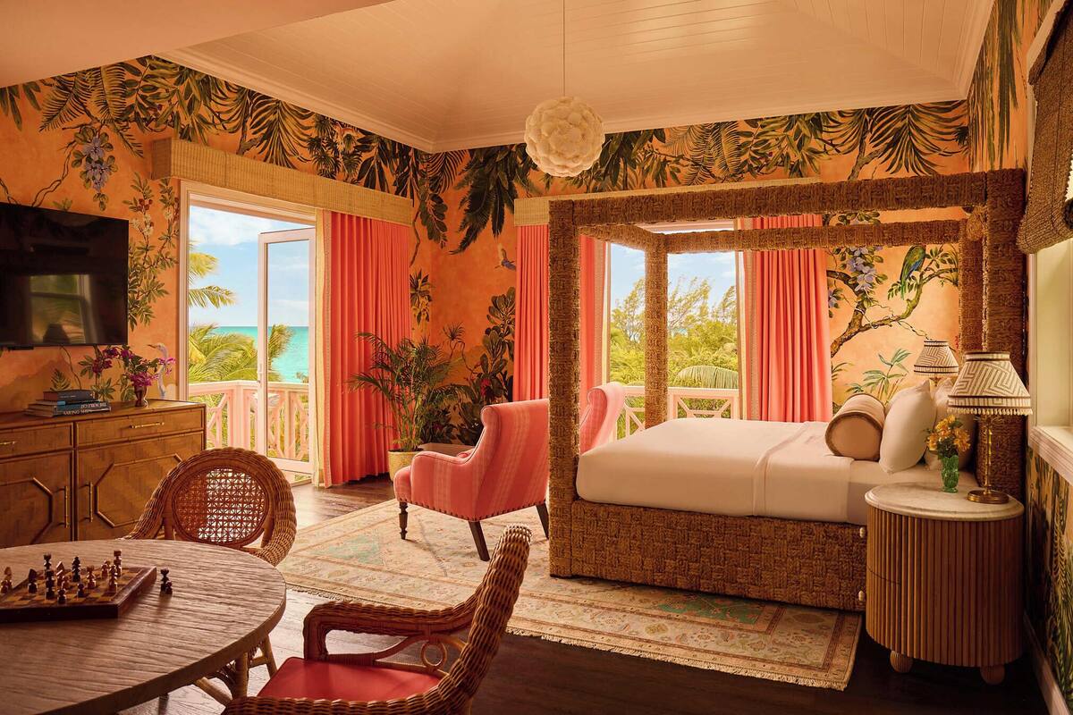 A tropical-themed bedroom with a four-poster bed, a television, a dining table with chess, and a view of the ocean.