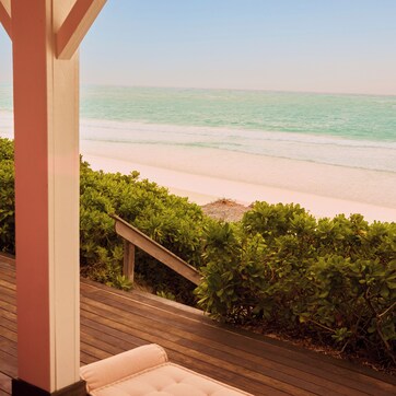 A wooden deck with a cushioned seating area overlooking a beach.