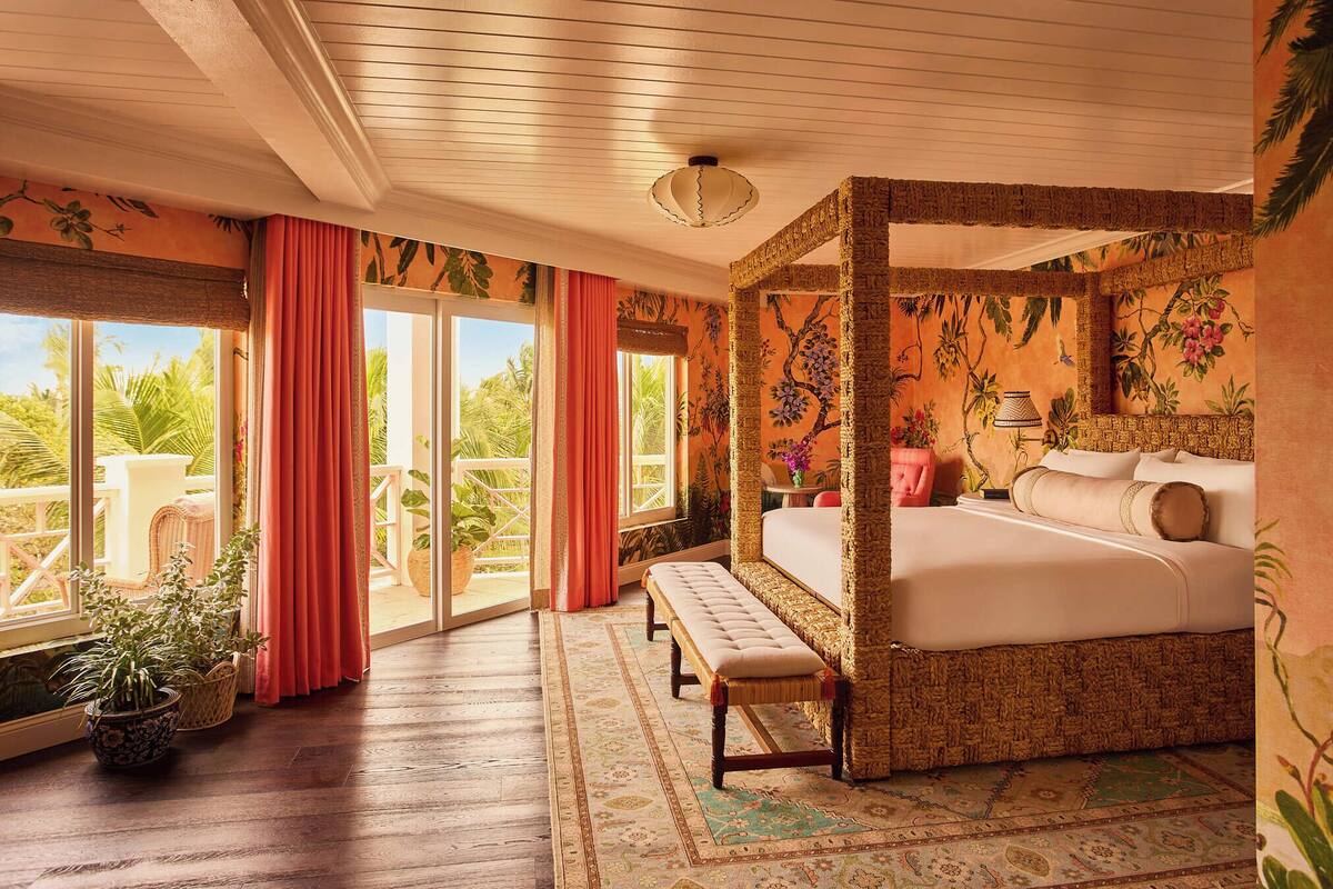 A spacious bedroom with a four-poster bed, a bench, and a view of the outdoors.