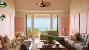 A spacious living room with a large window offering a view of the ocean, a ceiling fan, and a variety of seating options including a sofa and armchairs. - Coral Sands Inn & Cottages (Dunmore Town)