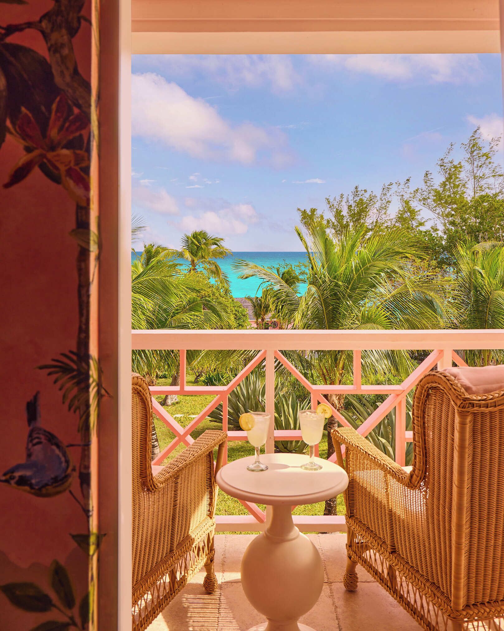 A balcony with wicker furniture, a table, and a view of the ocean.