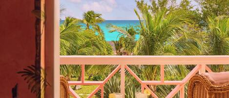 A balcony with wicker furniture, a table, and a view of the ocean.